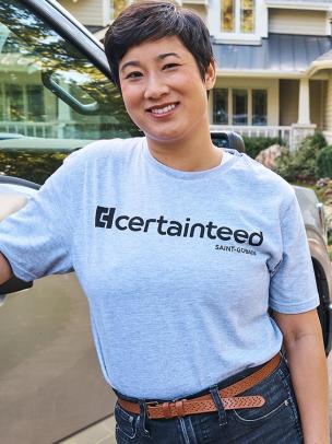 An Asian woman with a CertainTeed t-shirt smiling and leaning against a work truck.